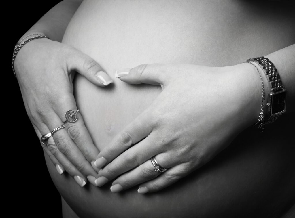 Närbild på gravidmage med händer mot svart bakgrund