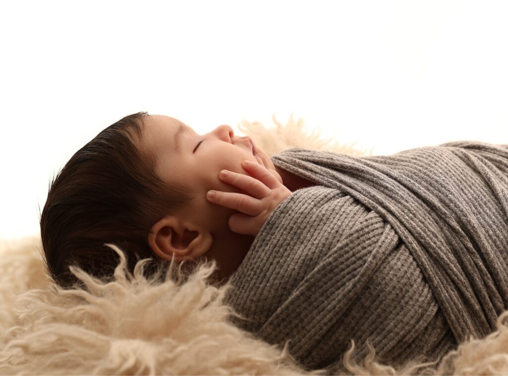 Nyfödd bebis ligger på ljus filt mot vit bakgrund