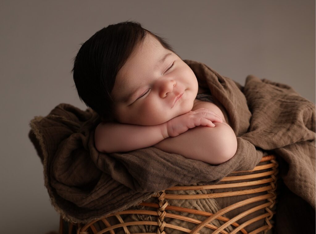 Sovande nyfödd bebis i korg mot grå bakgrund