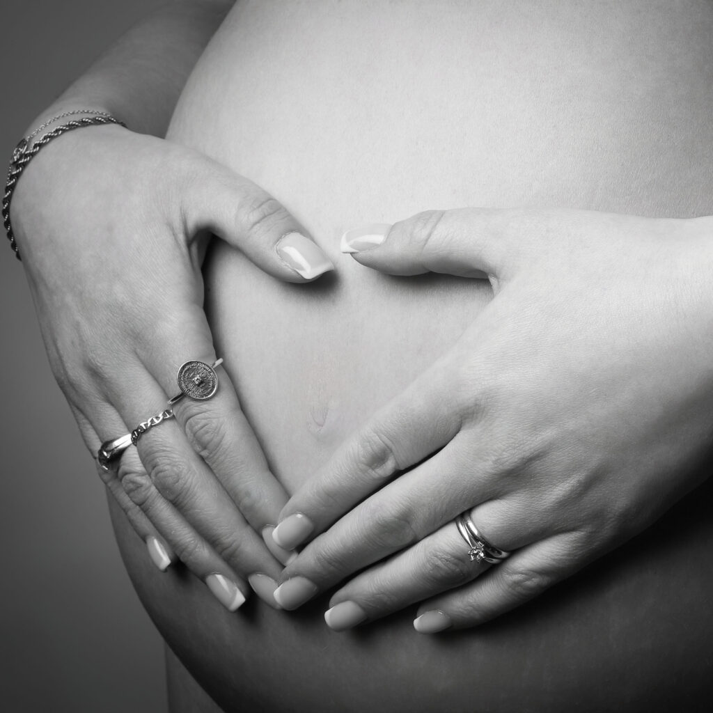 Händer formade som ett hjärta över gravidmage